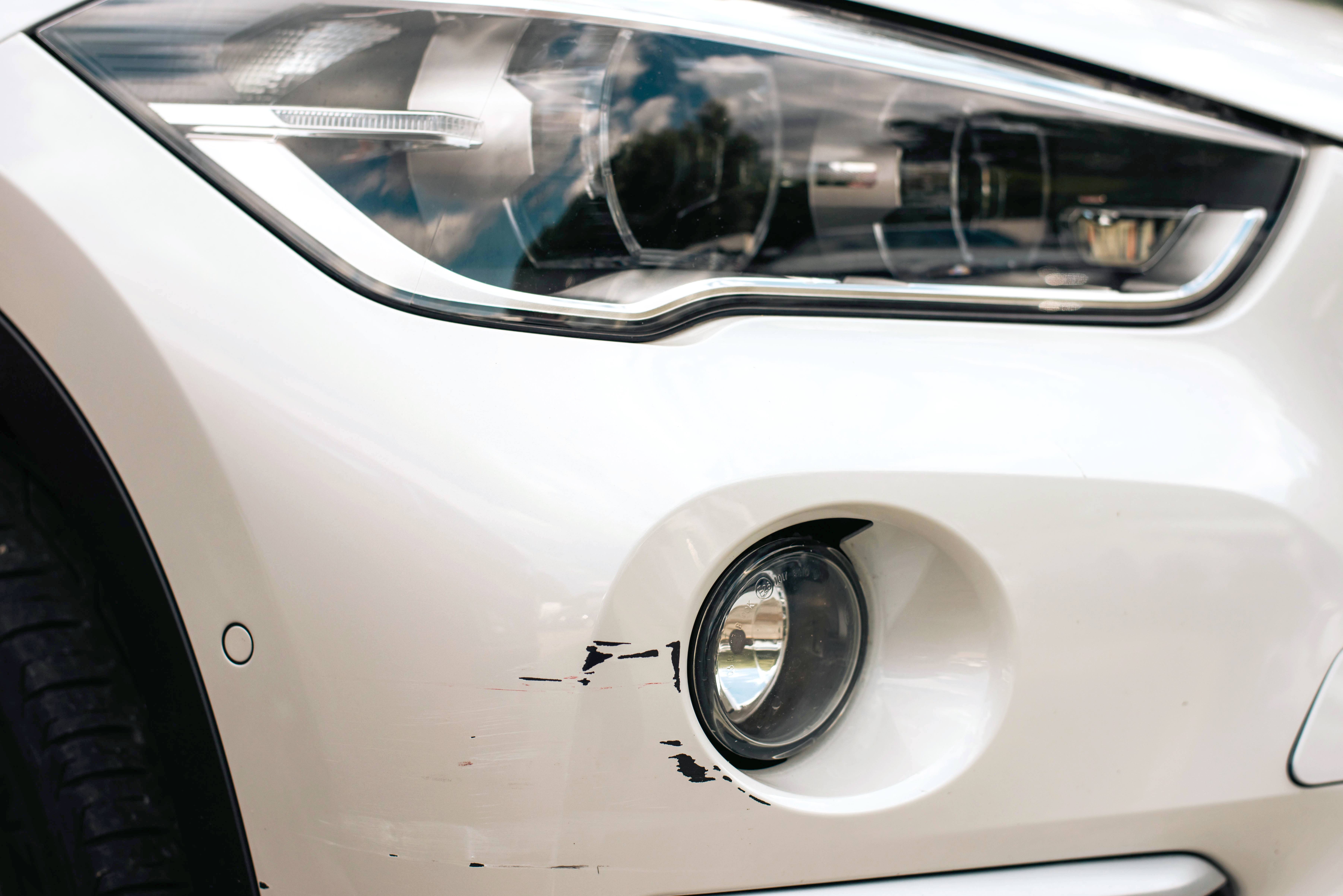 close up of a white car with minor scratch damage around one of the lights